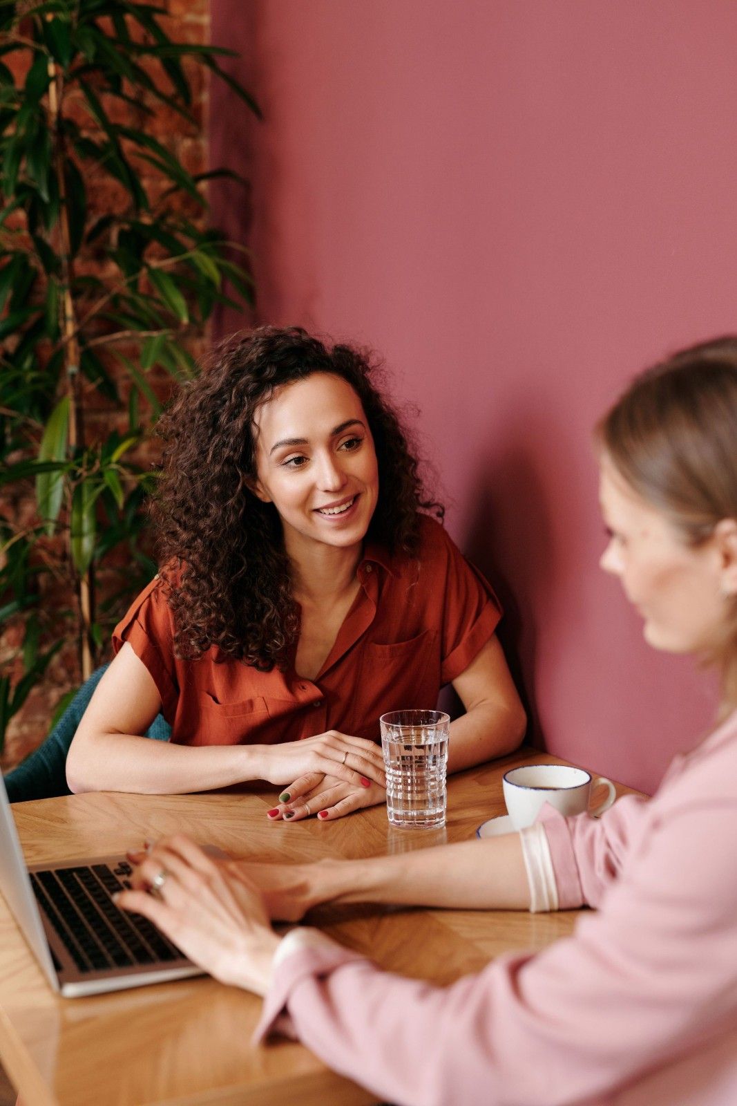 Two women engage in a collaborative discussion at a coffee shop table, sharing ideas and smiles.