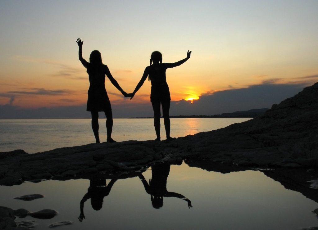 Two friends holding hands, silhouetted against a sunset on Sochumi beach, creating a serene and harmonious scene.