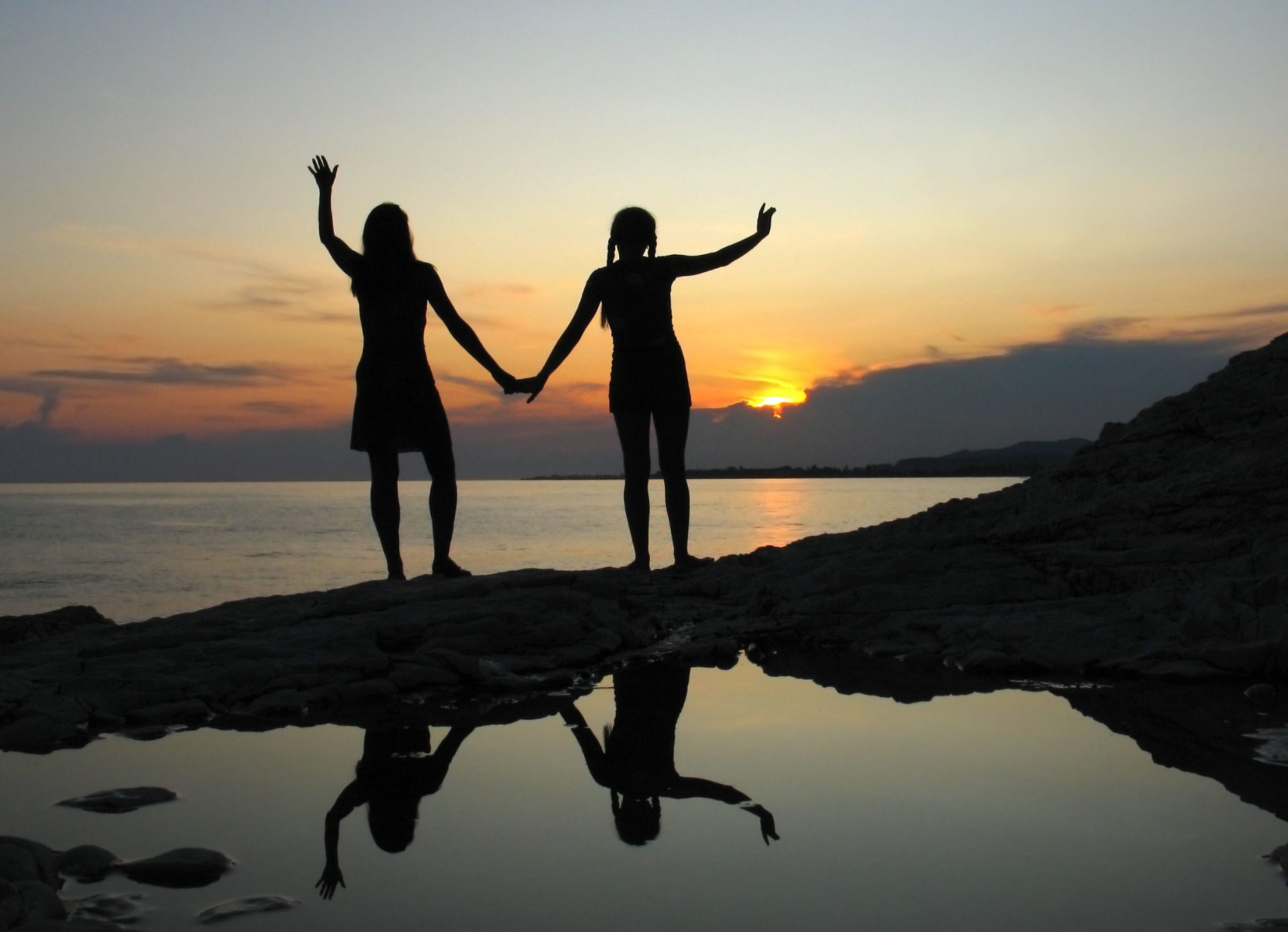 Two friends holding hands, silhouetted against a sunset on Sochumi beach, creating a serene and harmonious scene.